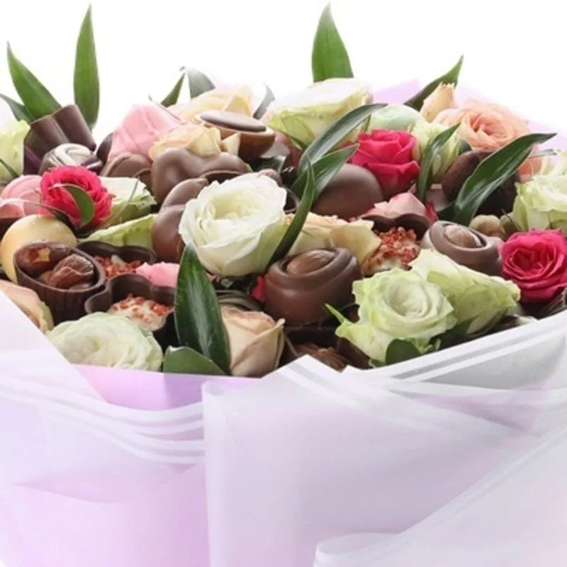 Bunter Blumen- und Schokoladenstrauß von MO BLUMEN mit weißen, rosa und roten Rosen, dazu Pralinen, in lila Papier gehüllt.